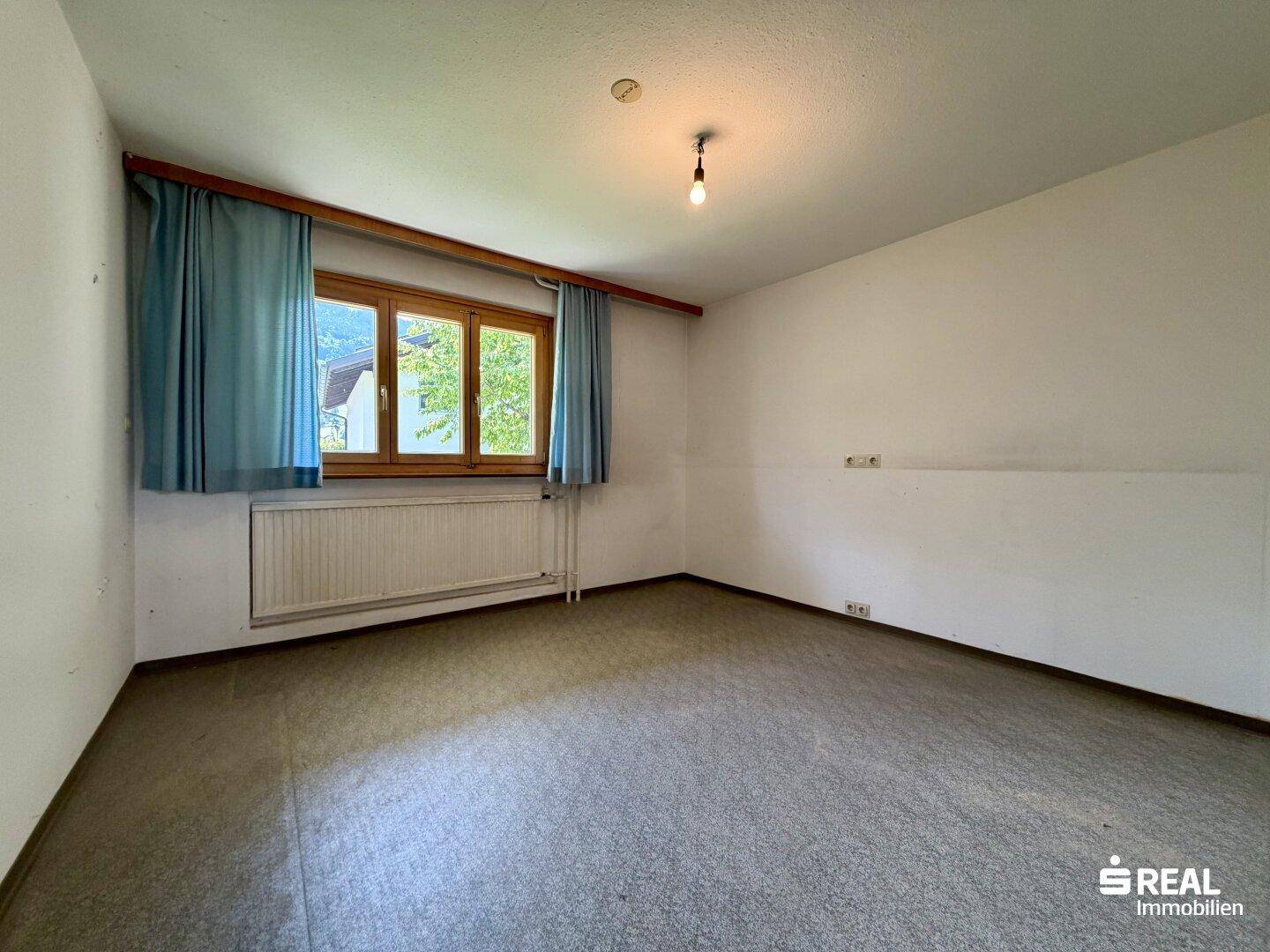 Schlafzimmer mit Teppichboden und Fenster, das einen Blick ins Grüne bietet.