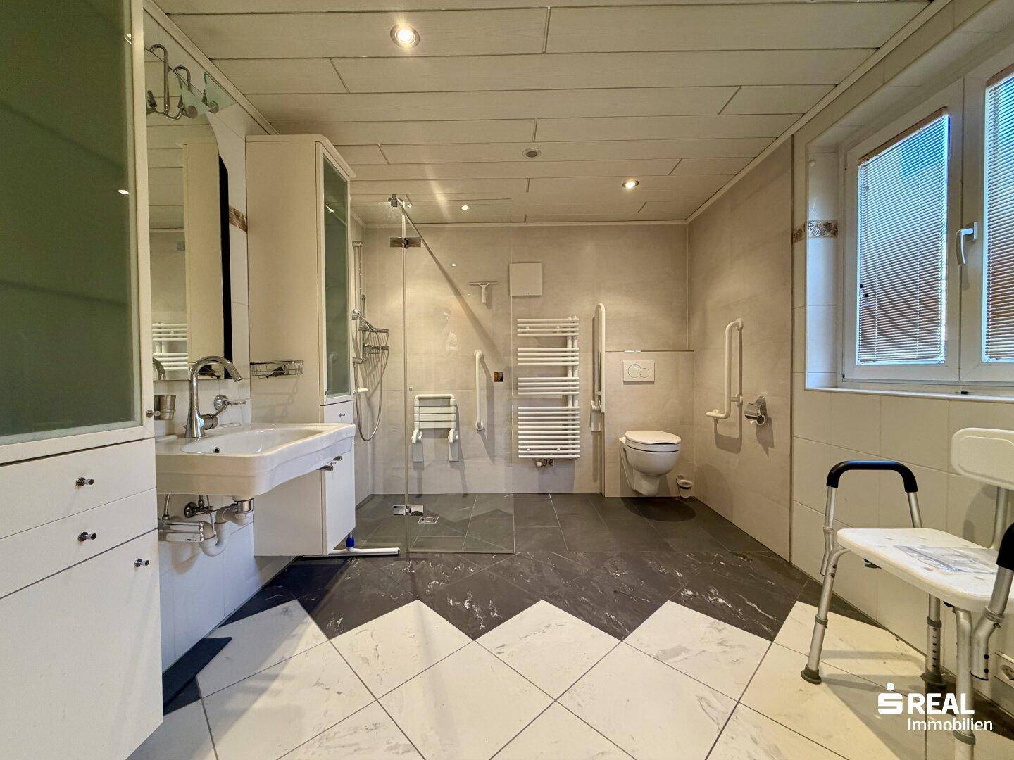 Modernisiertes Badezimmer mit ebenerdiger Dusche, Haltegriffen und stilvollen Bodenfliesen.