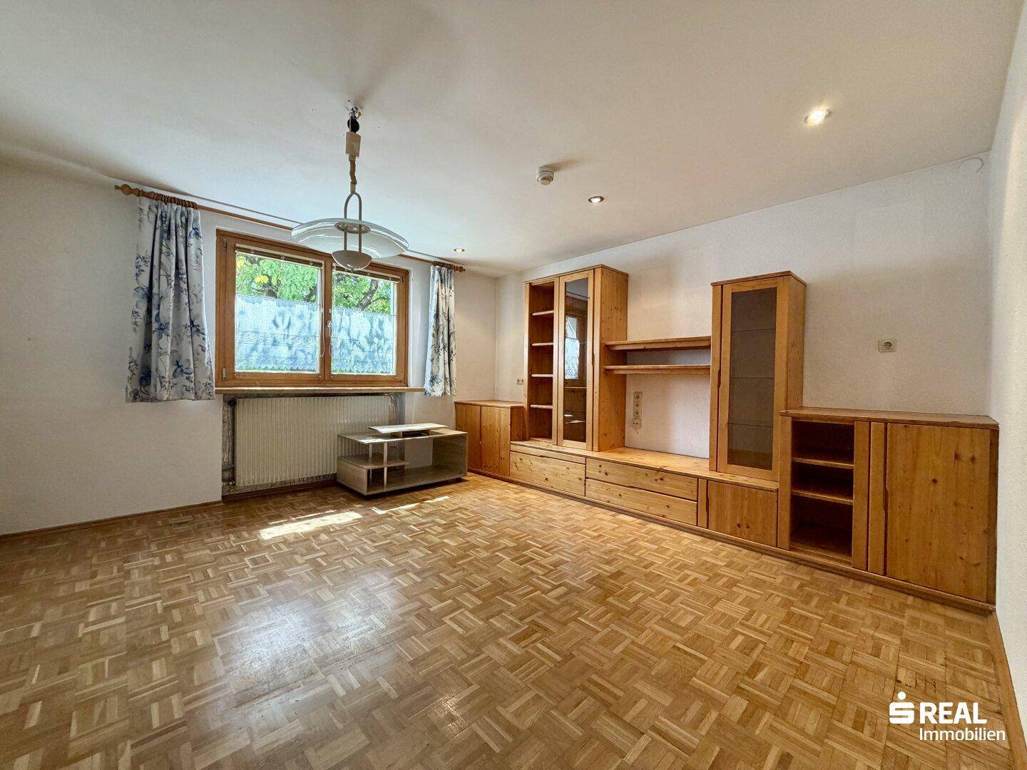 Wohnzimmer mit Fischgrätparkettboden und eingebauten Holzschränken, hell und geräumig.