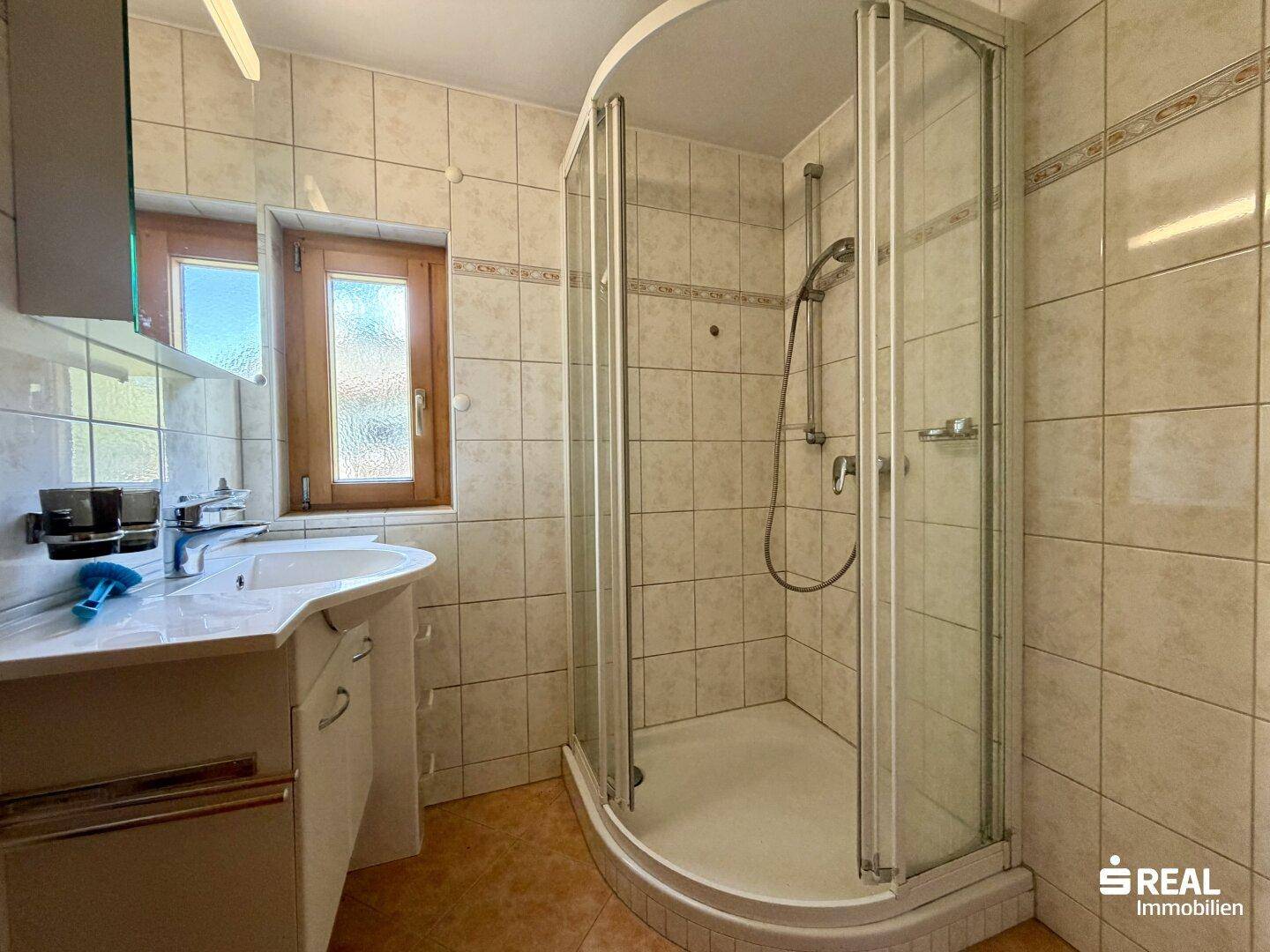 Badezimmer mit Eckdusche, Waschbecken und hellen Fliesen an den Wänden.