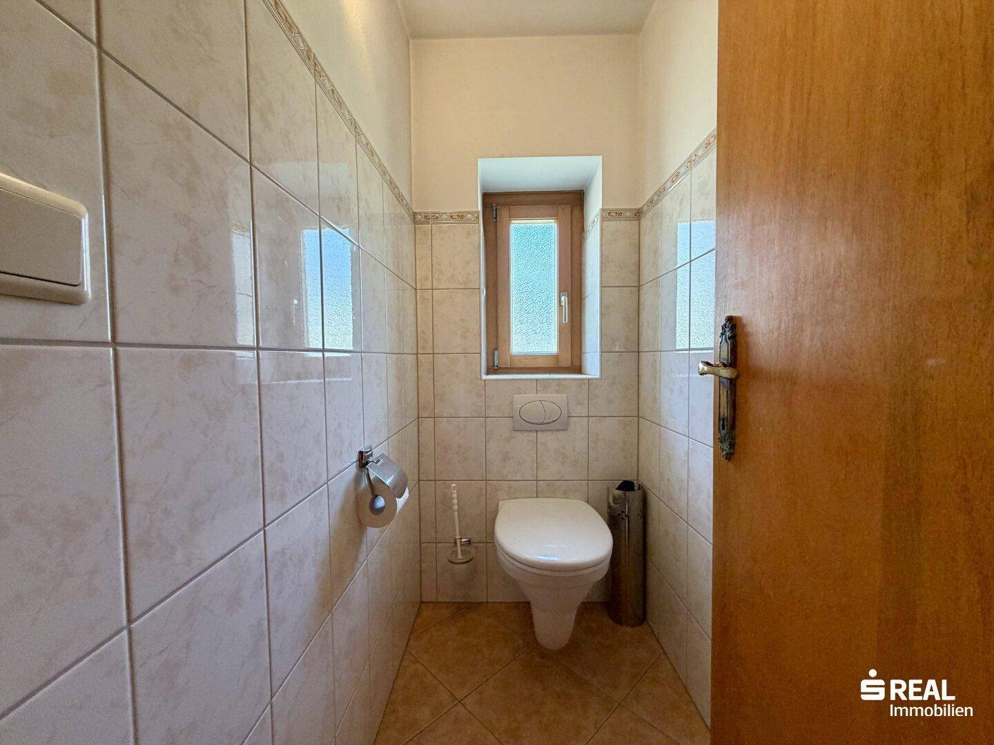 Separates WC mit hellen Fliesen und einem kleinen Fenster für Tageslicht.
