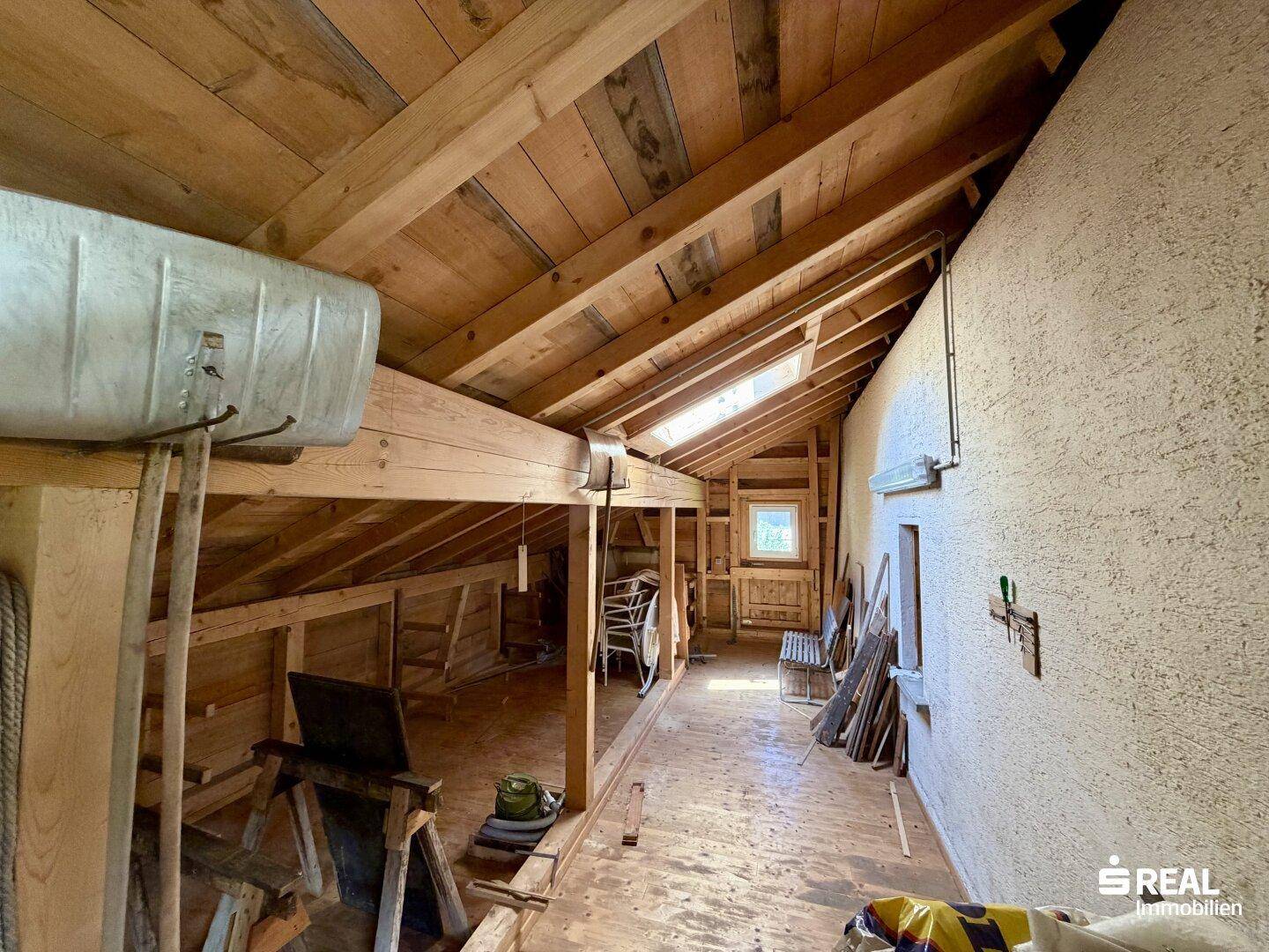 Unausgebauter Dachboden mit sichtbaren Holzbalken und Dachfenster, viel Potenzial.