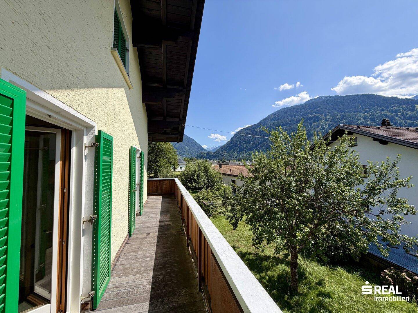 Langer Holzbalkon mit Bergblick und grünen Fensterläden, ideal zum Entspannen.