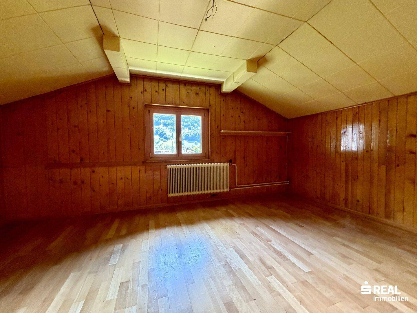 Dachzimmer mit Holzvertäfelung, schrägen Decken und Holzboden, gemütlich und hell.