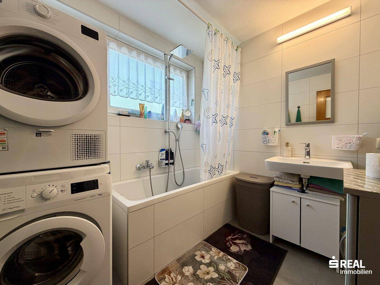 Badezimmer mit Badewanne, Duschvorhang, Waschmaschine und Trockner.