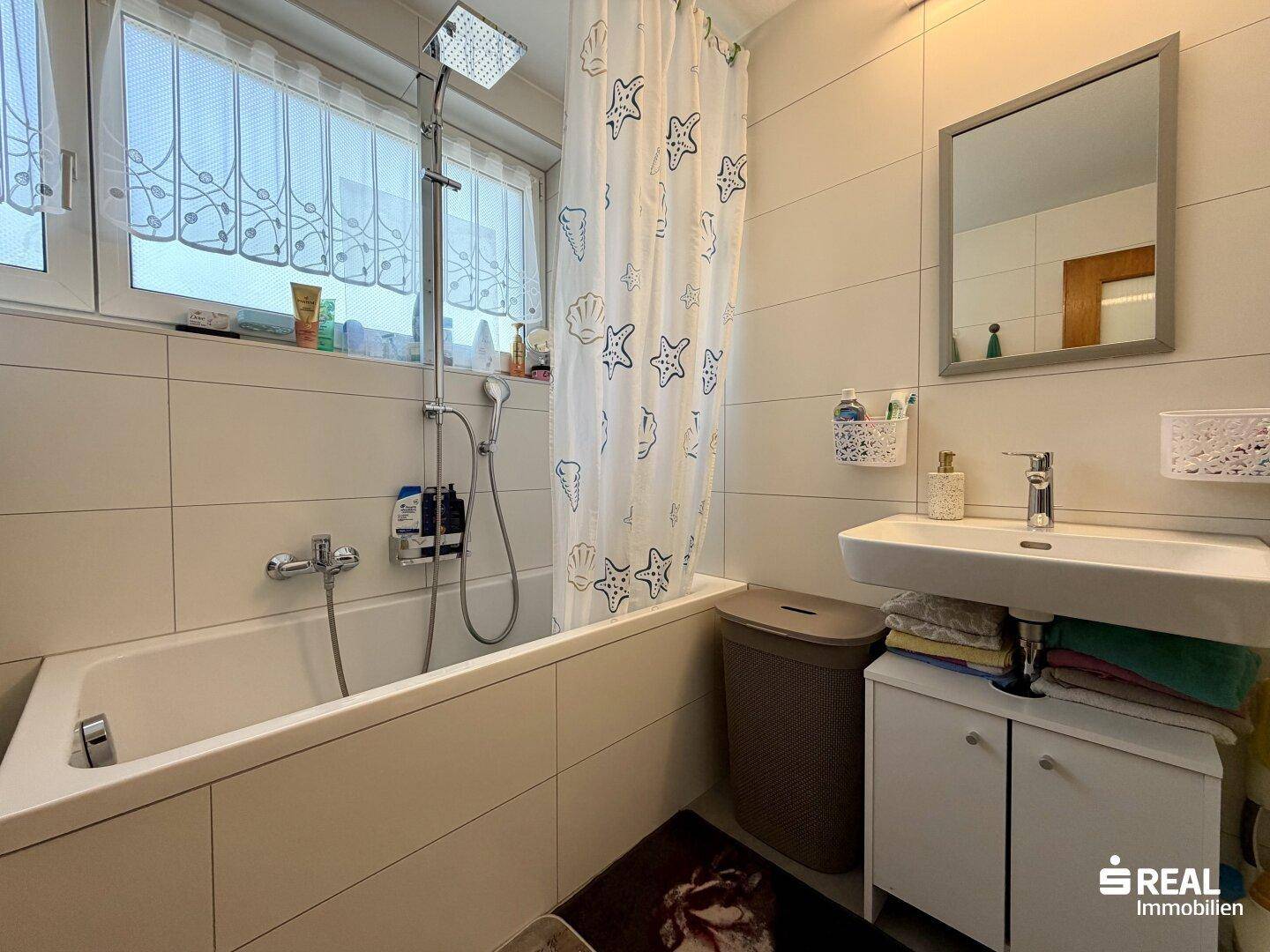 Badezimmer mit Badewanne, Duschvorhang, Waschbecken und Fenster für Tageslicht.