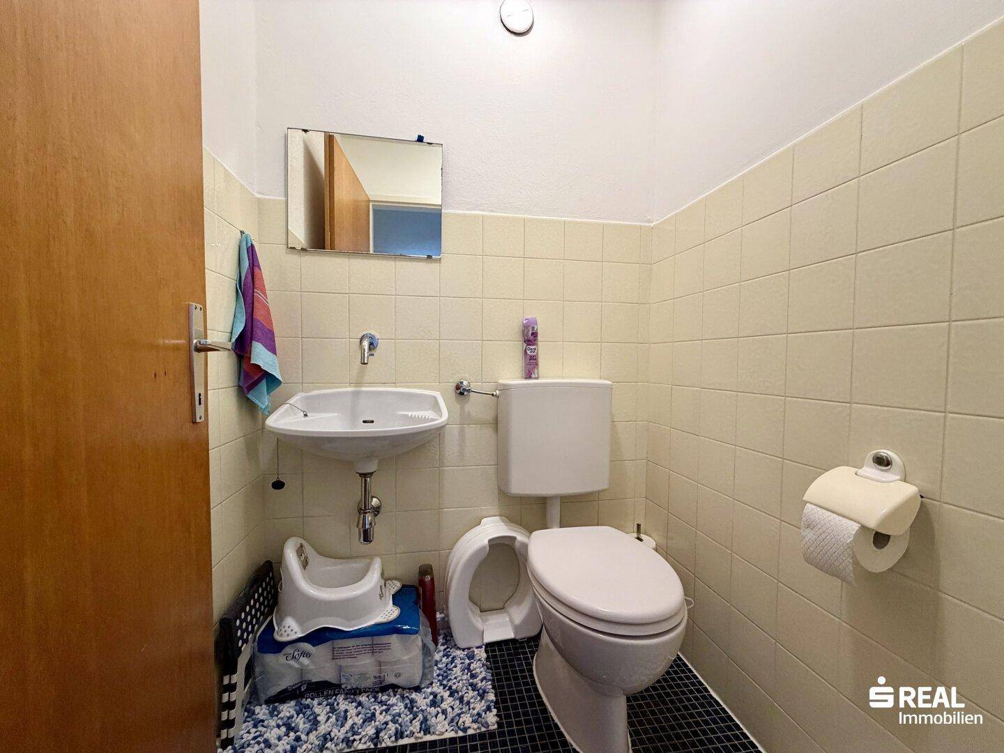 Separate Toilette mit Waschbecken und hellen Fliesen an den Wänden.