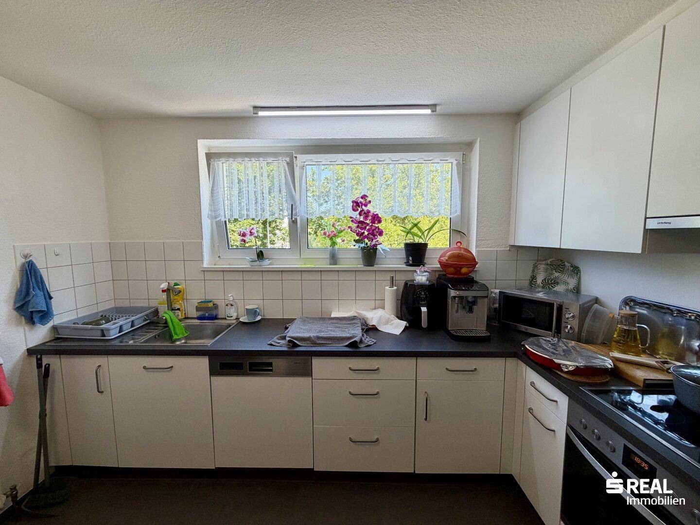 Funktionale Küche mit weißen Schränken, dunkler Arbeitsplatte und Fenster.