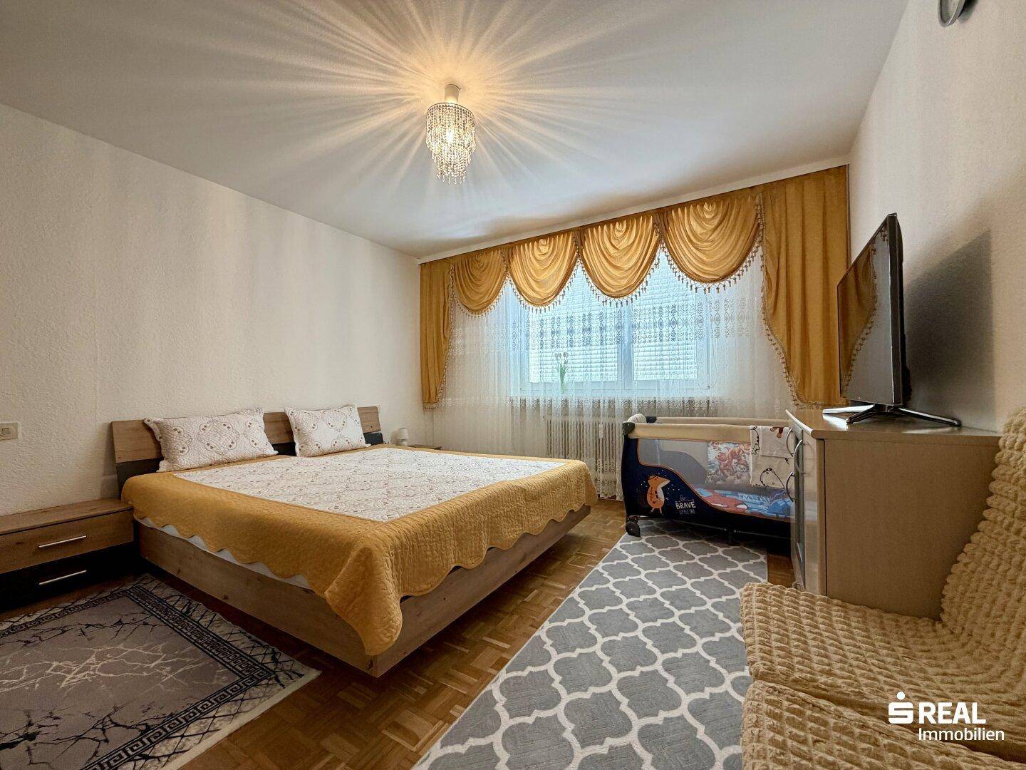 Gemütliches Schlafzimmer mit Doppelbett, Teppich und Vorhängen in warmen Farbtönen.