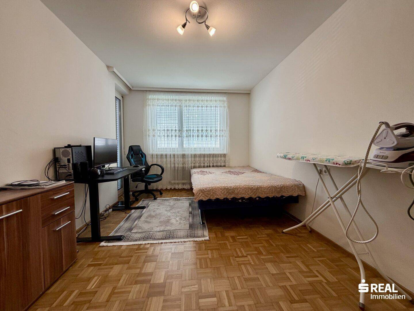 Einfaches Schlafzimmer mit Einzelbett, Schreibtisch und Parkettboden.
