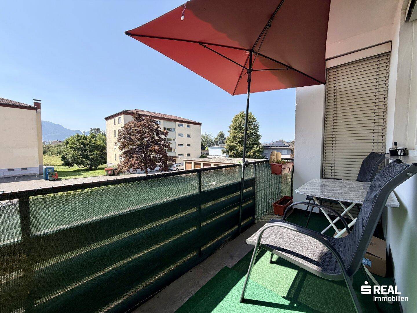 Möblierter Balkon mit Sonnenschirm und Blick auf die Umgebung.