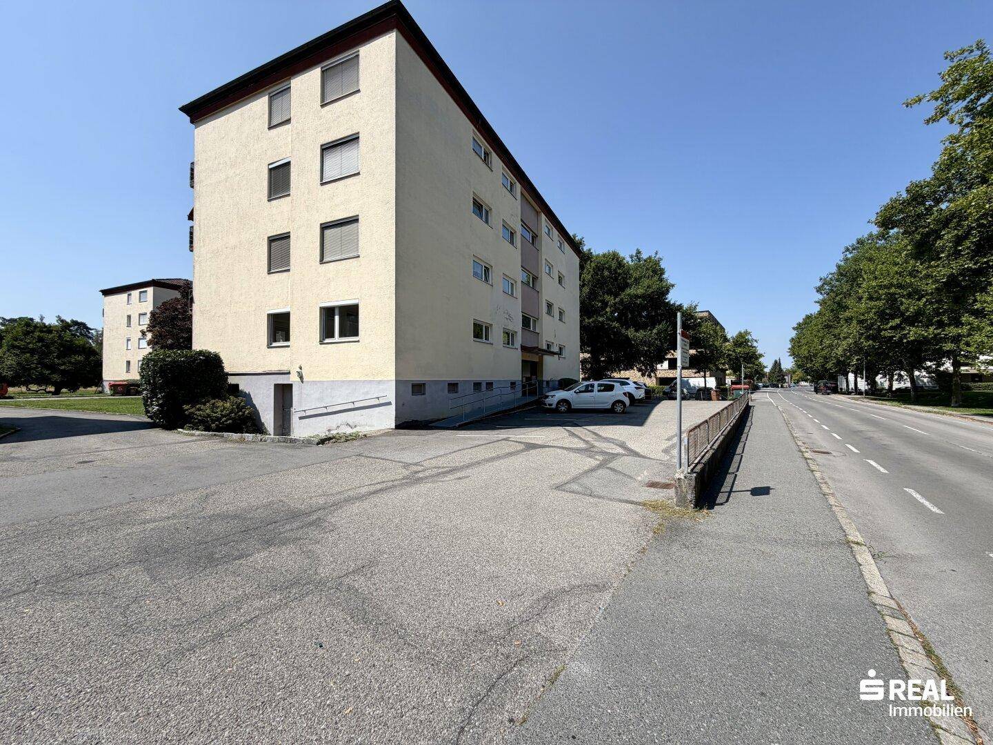 Mehrfamilienhaus an einer Straße mit Parkplätzen und Bäumen.