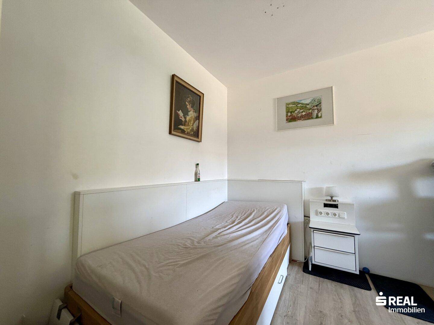 Helles Schlafzimmer mit Einzelbett, Nachttisch und schlichter Einrichtung.