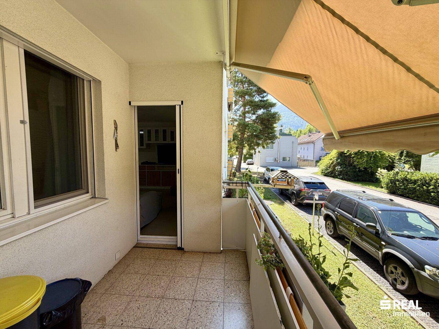 Balkon mit Zugang zum Innenbereich und Blick auf die Straße mit parkenden Autos.