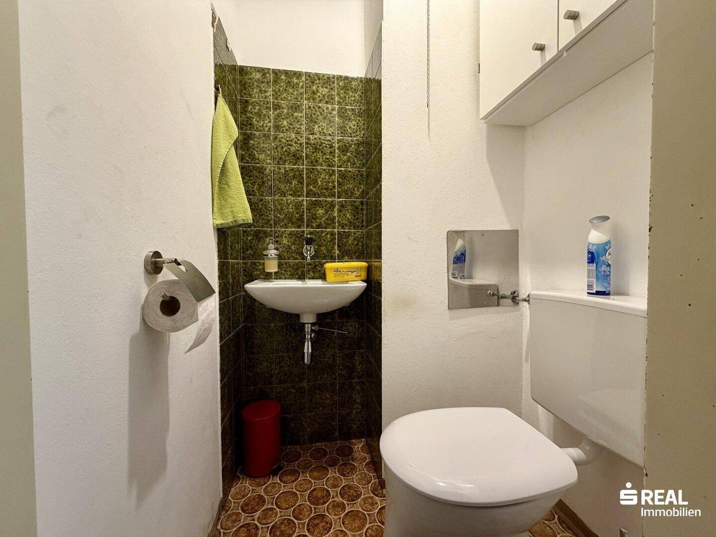 Kleines Gäste-WC mit grünen Fliesen, Toilette und Handwaschbecken.