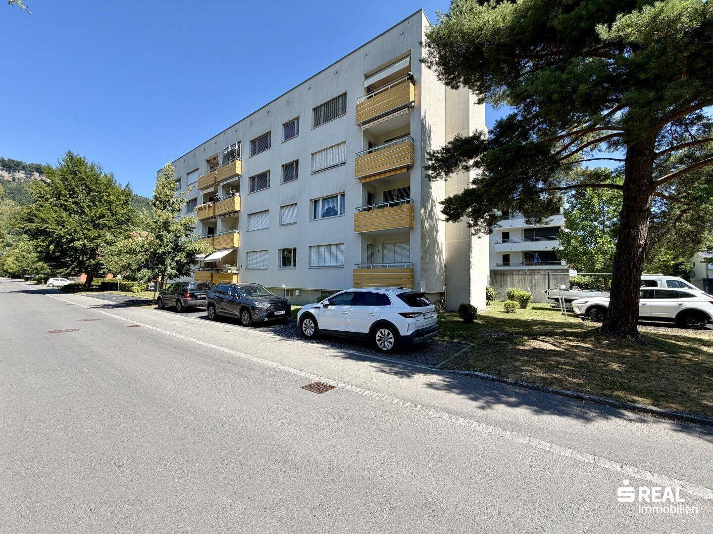 Ansicht des Mehrfamilienhauses von der Straßenseite mit Balkonen und parkenden Autos.