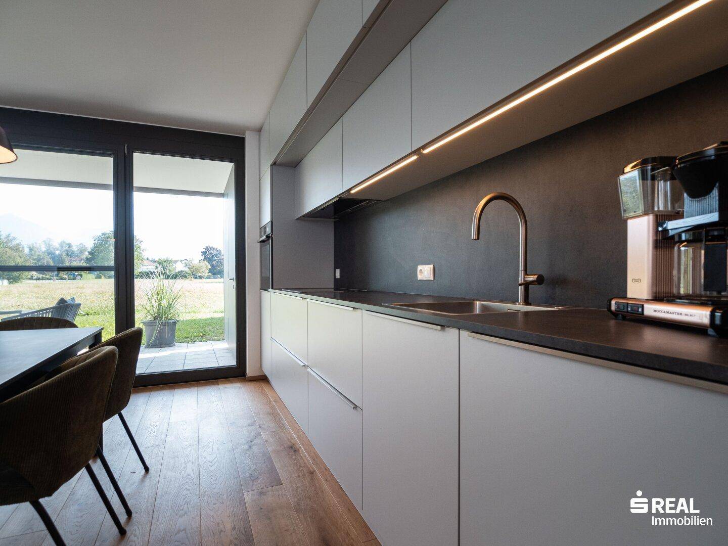 Moderne Einbauküche mit dunkler Arbeitsplatte, Spüle und Kaffeemaschine.