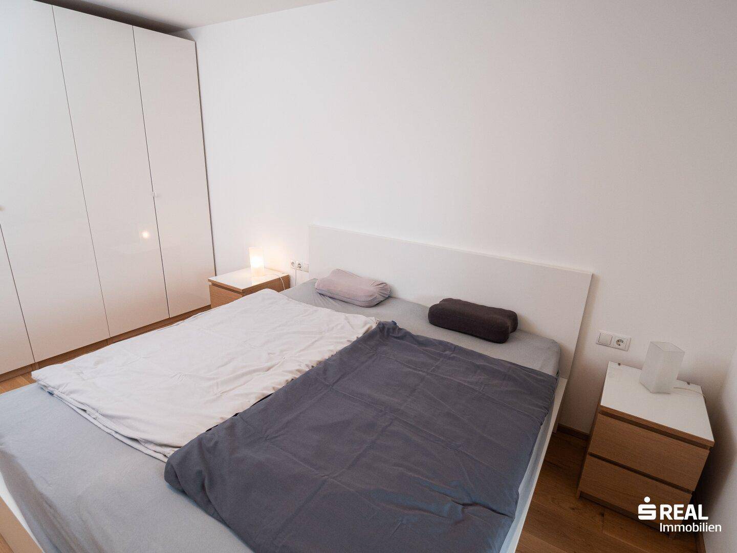 Helles Schlafzimmer mit großem Bett, weißen Einbauschränken und Holzboden.