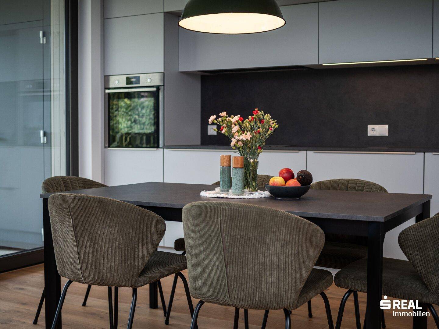 Moderne Küche mit dunkler Arbeitsplatte, integriertem Backofen und frischen Blumen.