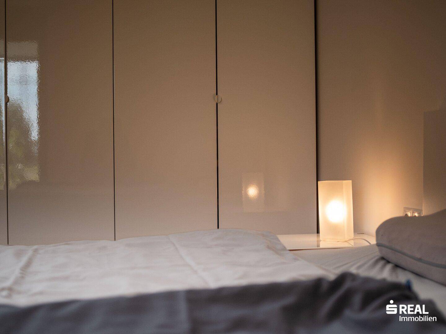 Nahaufnahme des Bettes und der weißen Schränke im Schlafzimmer mit Nachttischlampe.