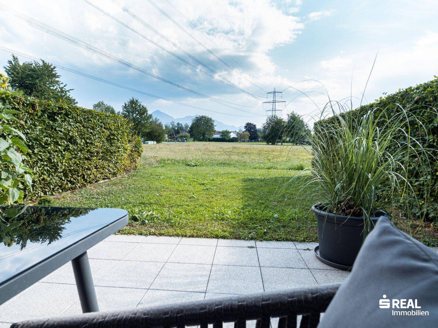 Terrasse mit Blick auf eine weite Grünfläche und Berge im Hintergrund.