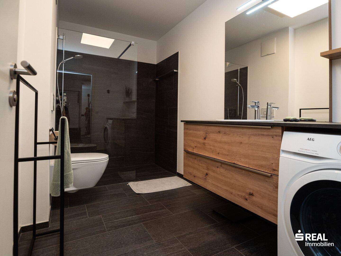 Modernes Badezimmer mit begehbarer Dusche, Holzwaschtisch und Waschmaschine.