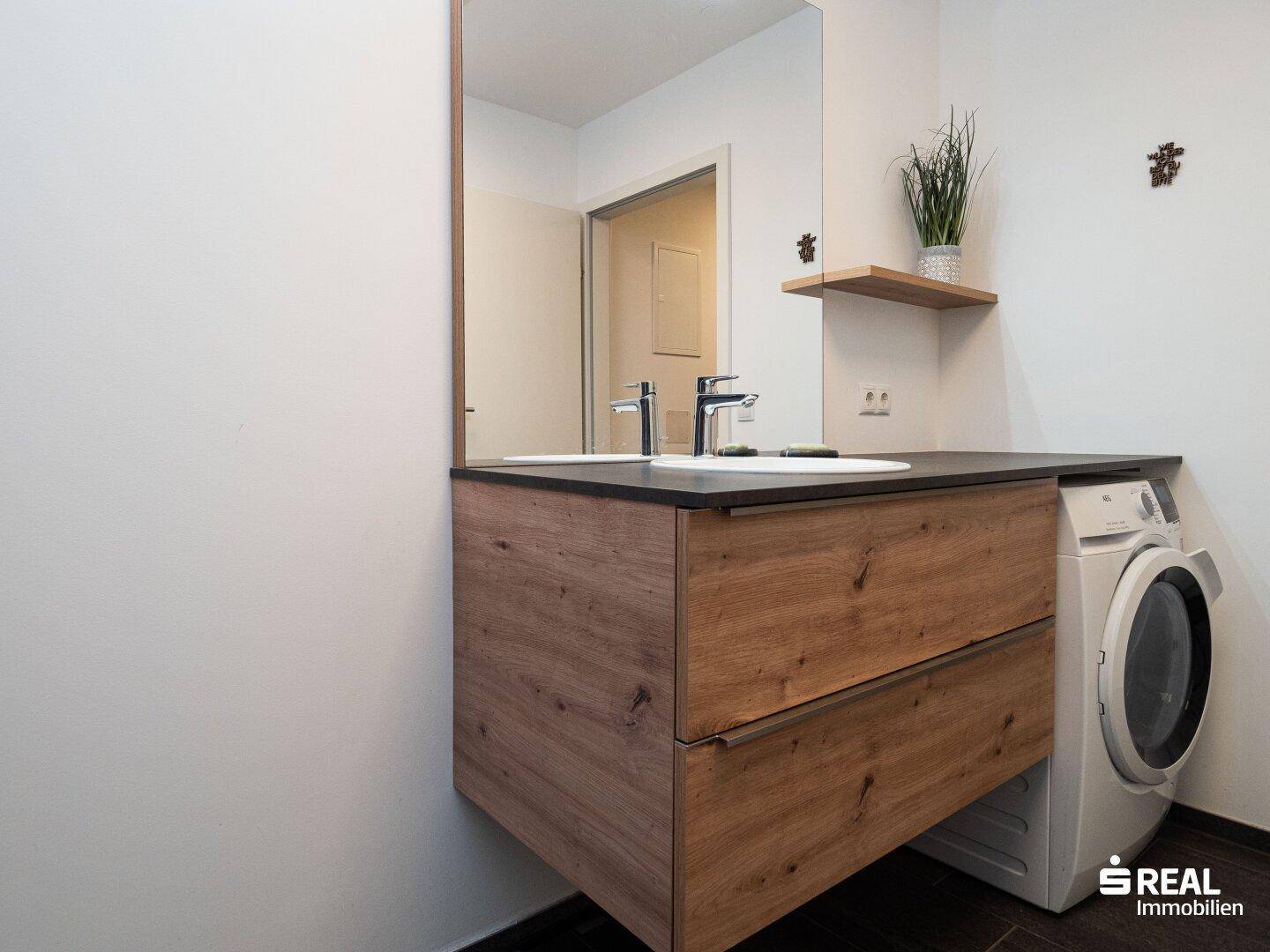 Badezimmer mit modernem Holzwaschtisch, Spiegel und integrierter Waschmaschine.