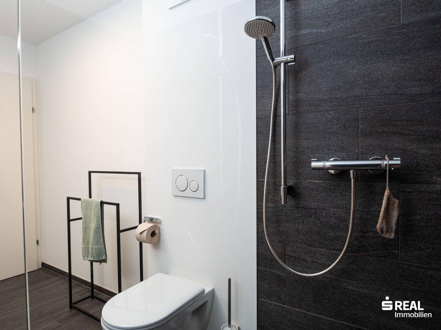 Detaillierte Ansicht der modernen Dusche und des wandhängenden WCs im Badezimmer.