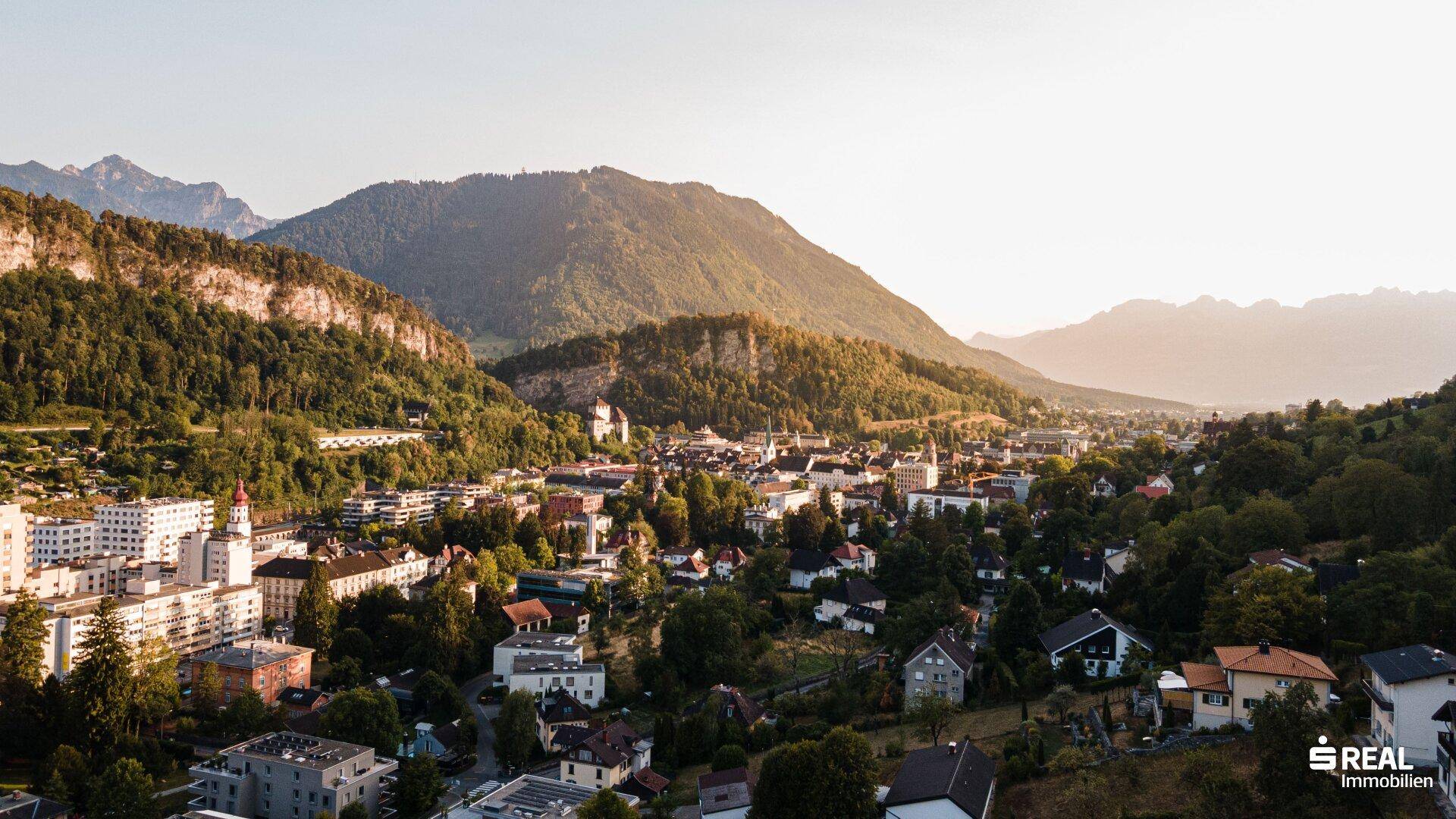 Malerischer Panoramablick auf eine Stadt im Tal, umrahmt von majestätischen Bergen im warmen Abendlicht.