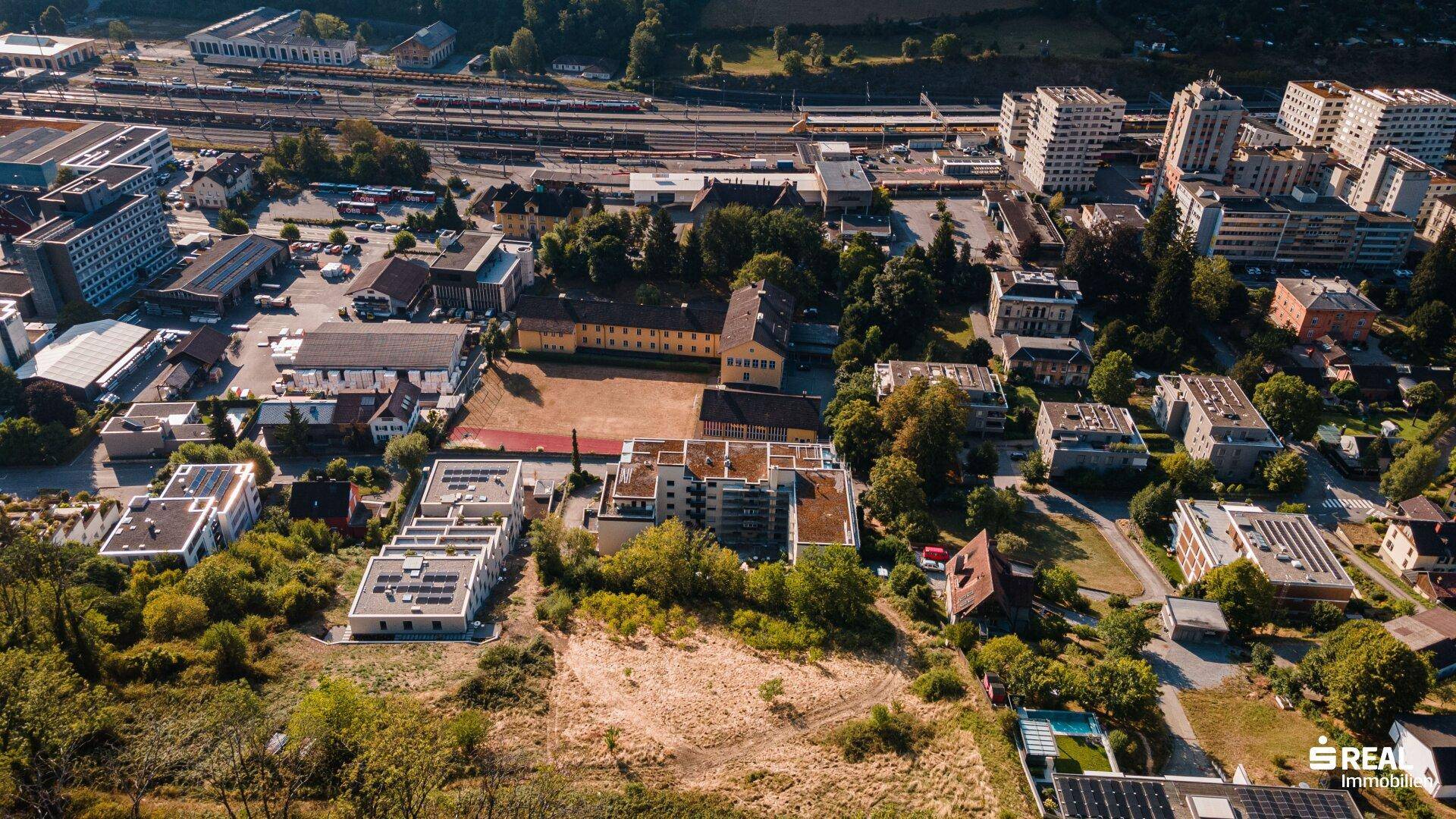 Weitläufige Luftaufnahme einer Stadt mit Wohngebieten, Gewerbeflächen und einem Bahnhof im Hintergrund.
