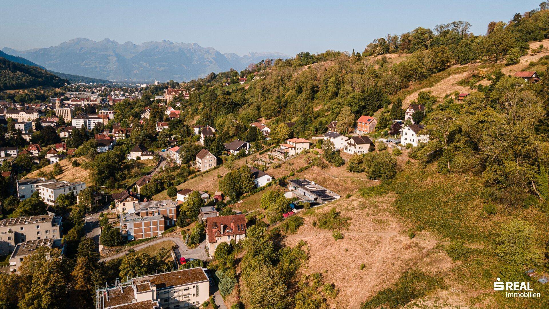 Weitläufige Luftaufnahme einer Siedlung am Hang mit Blick auf die umliegende Berglandschaft.