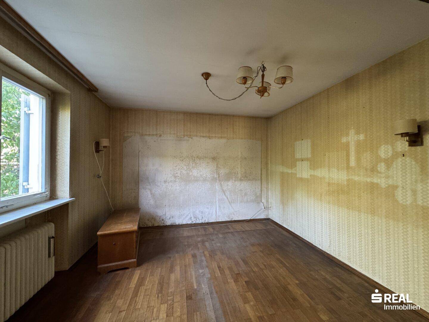 Zimmer mit Parkettboden und abgenutzter Tapete, bereit für eine Renovierung.