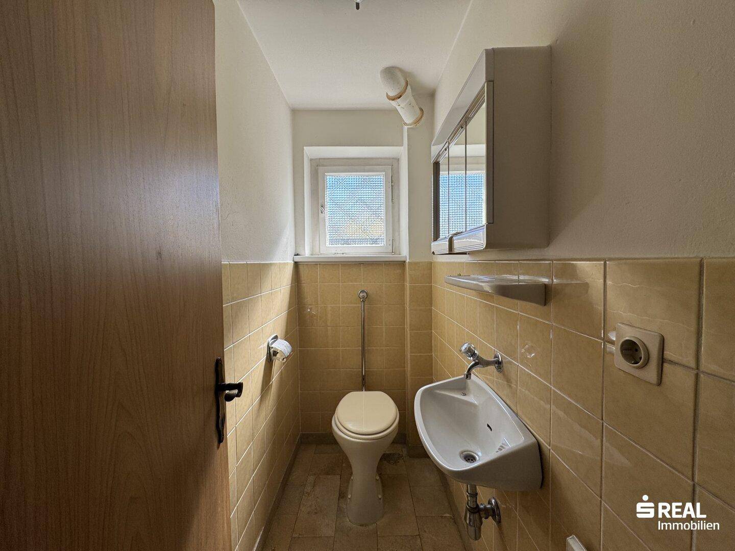 Kleines Gäste-WC mit gelben Fliesen, Toilette, Waschbecken und Fenster.