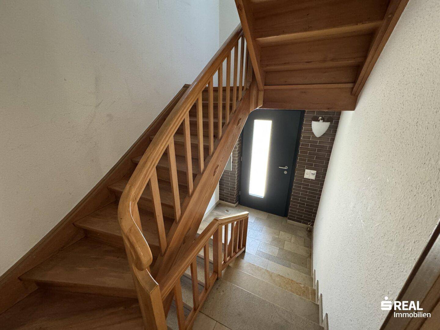 Holztreppe führt in die obere Etage, mit gefliestem Eingangsbereich und Haustür.