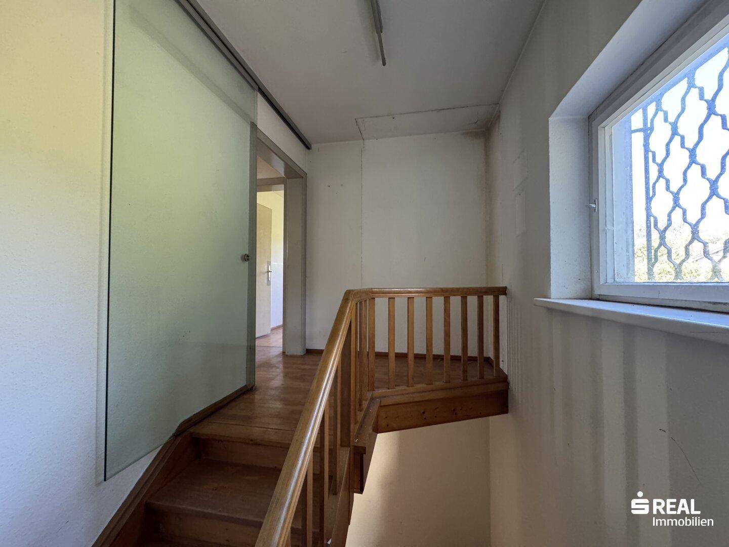 Holztreppe mit Glas-Schiebetür, die zu den oberen Räumen führt.