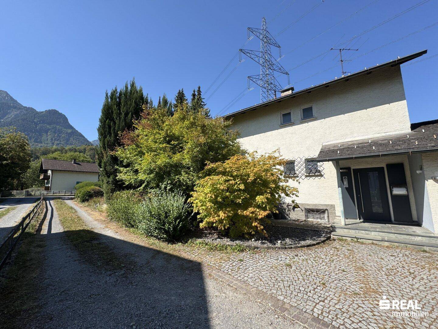 Fassade des Hauses mit gepflasterter Auffahrt und üppiger Bepflanzung im Vorgarten.