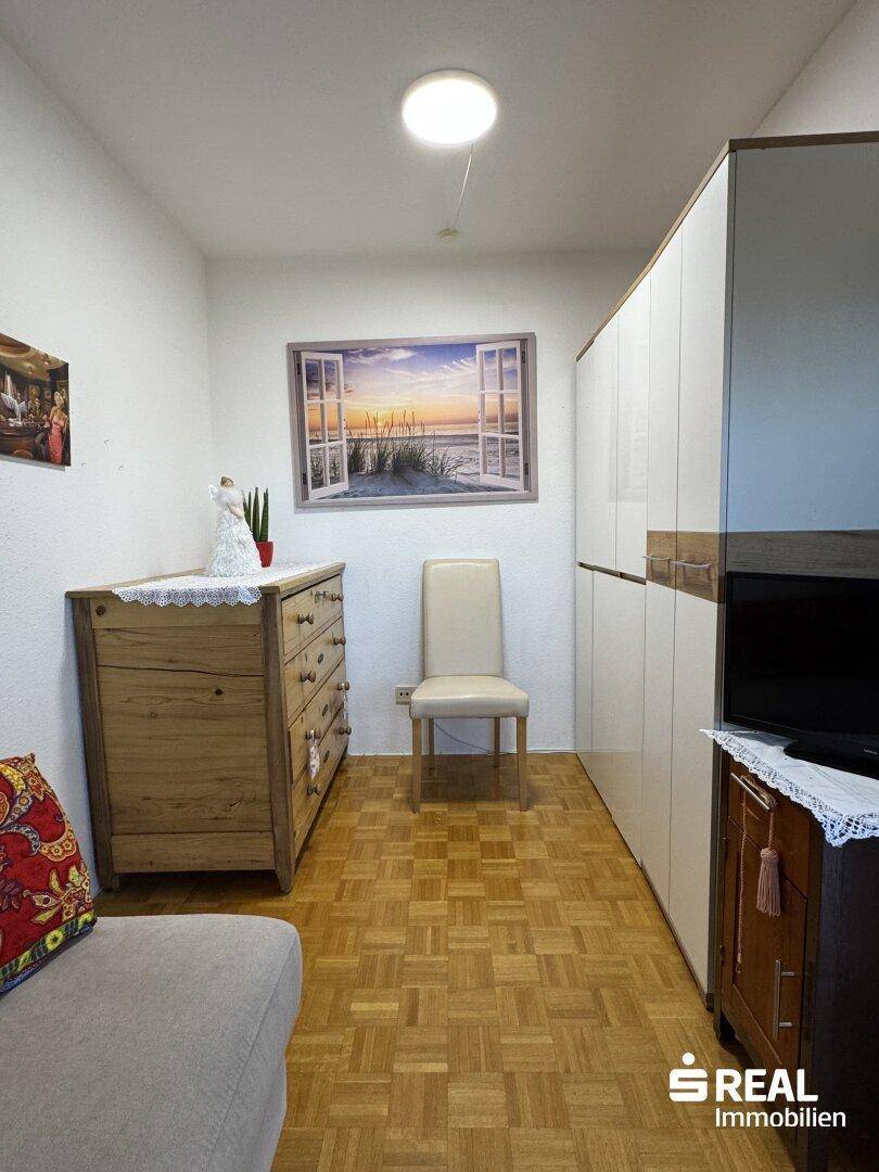 Schlafzimmer mit Parkettboden, großem Kleiderschrank und einer Kommode.