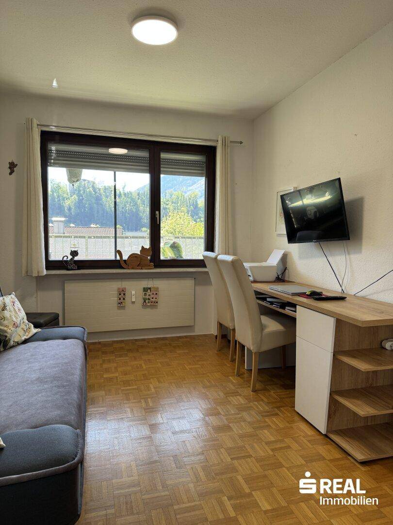 Helles Arbeitszimmer mit Schreibtisch, Sofa und Blick auf die grüne Umgebung.