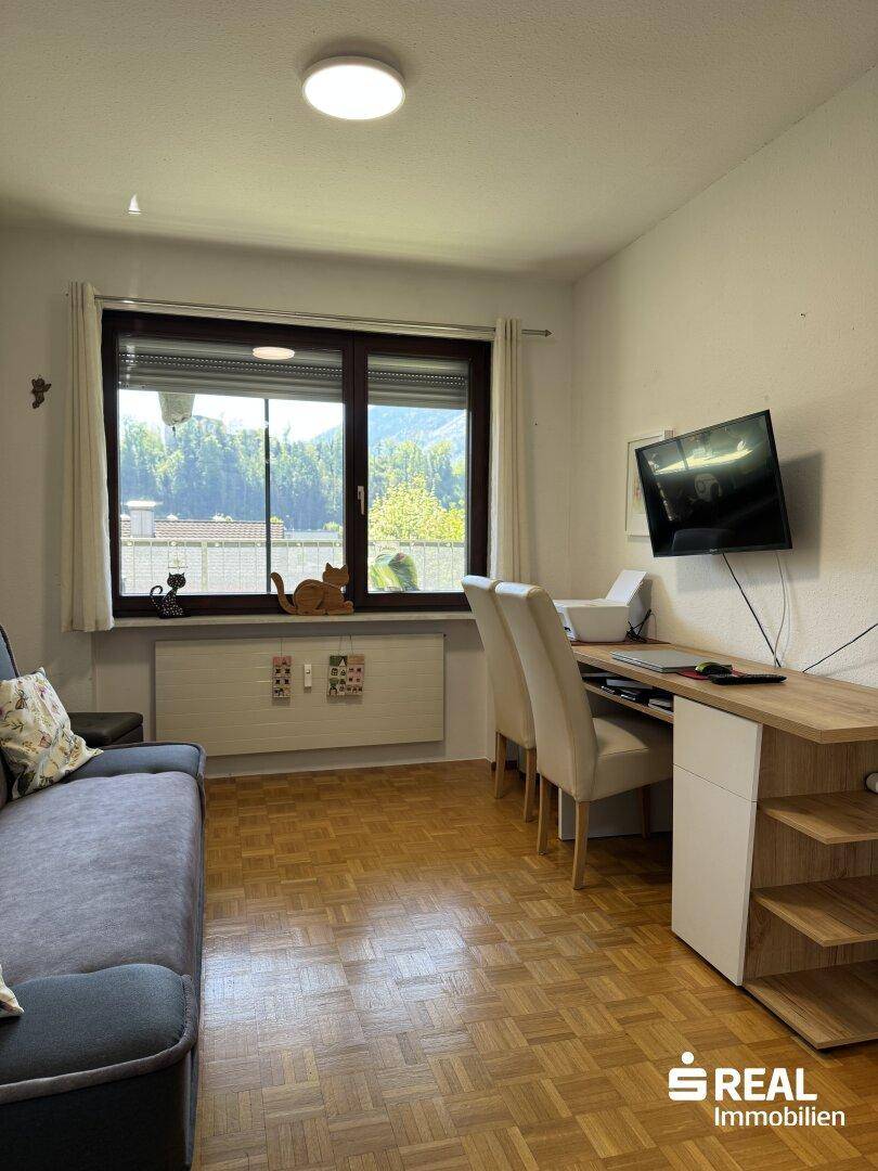 Funktionales Arbeitszimmer mit Schreibtisch, bequemer Couch und Blick ins Grüne.