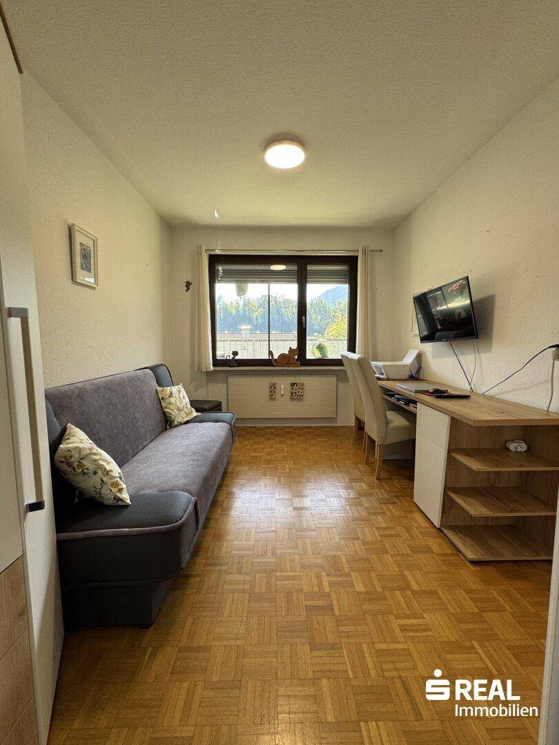 Helles Arbeitszimmer mit Schreibtisch, Sofa und Blick auf die grüne Umgebung.