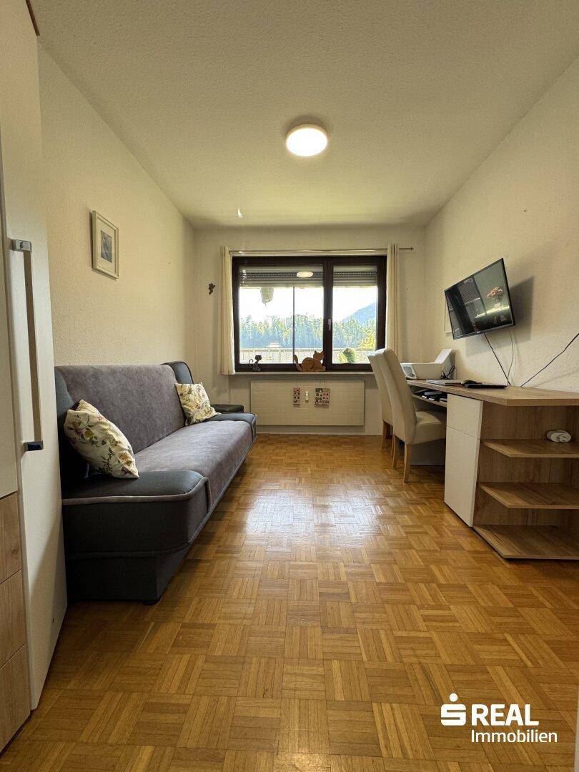 Funktionales Arbeitszimmer mit Schreibtisch, bequemer Couch und Blick ins Grüne.