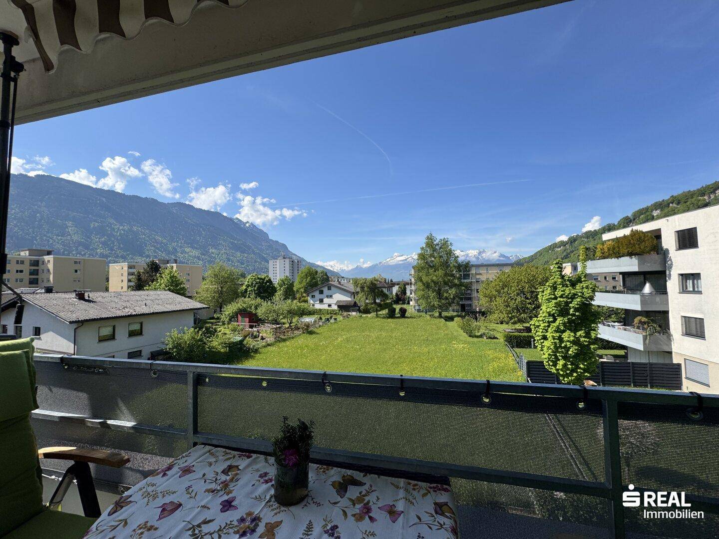 Panoramablick vom Balkon über eine weite Grünfläche und die majestätischen Berge.