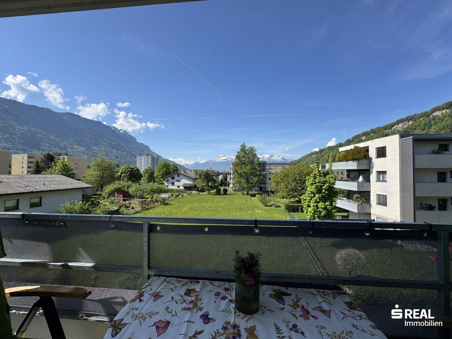 Weitläufiger Blick vom Balkon auf eine grüne Wiese und die umliegende Berglandschaft.