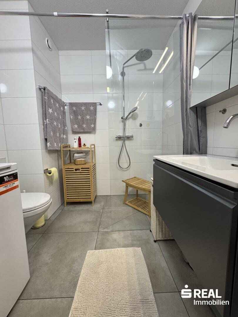 Helles Badezimmer mit moderner Dusche, Einzelwaschbecken und praktischem Stauraum.