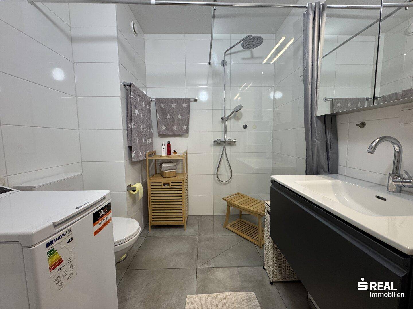Funktionales Badezimmer mit Dusche, Waschbecken und integrierter Waschmaschine.