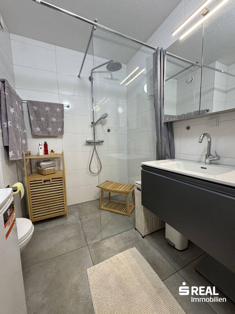 Modernes Badezimmer mit großer begehbarer Dusche, Einzelwaschbecken und grauen Fliesen.