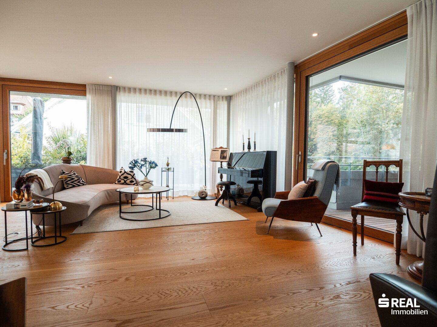 Heller Wohnbereich mit beigem Sofa, Holzboden und großzügigen Fenstern.