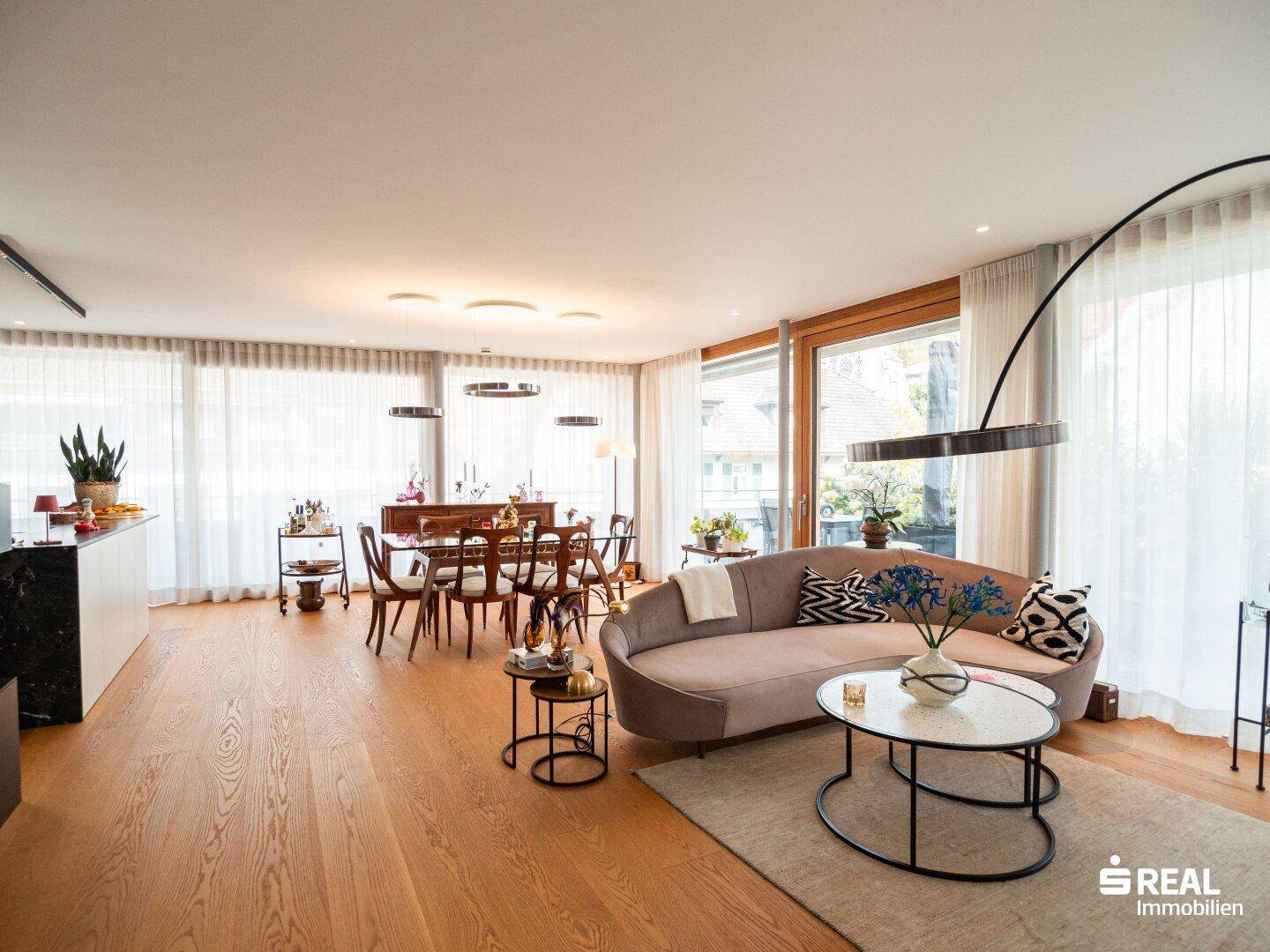 Geräumiger Wohnbereich mit beigem Sofa, Holzboden und Essbereich im Hintergrund.