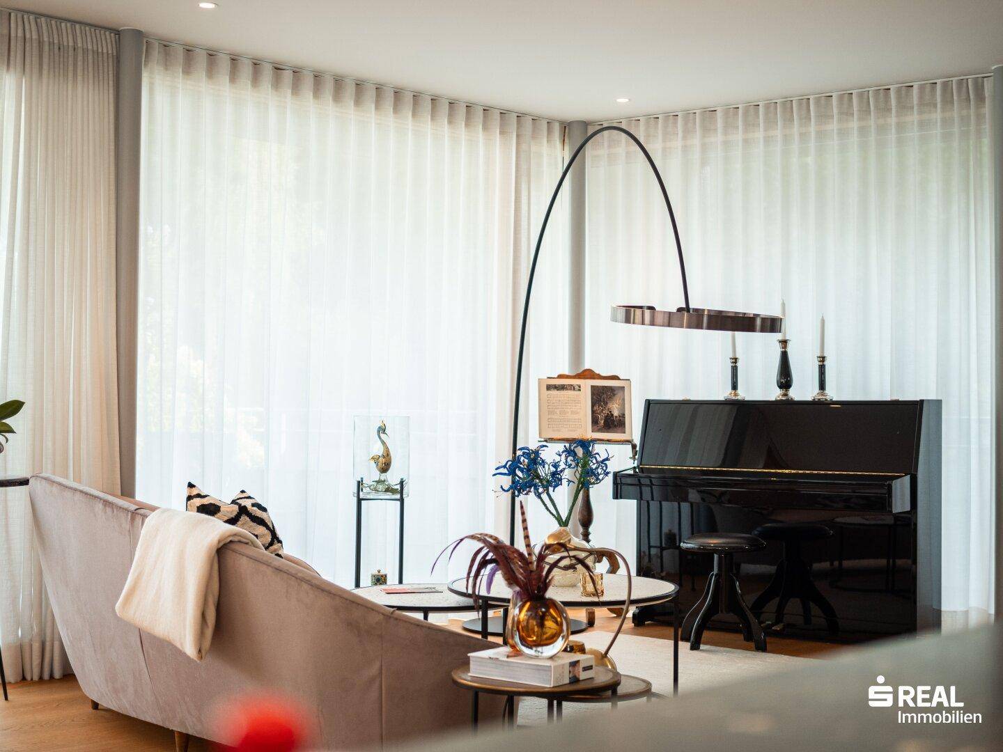Detailansicht des Wohnzimmers mit elegantem Sofa, Klavier und moderner Bogenlampe.