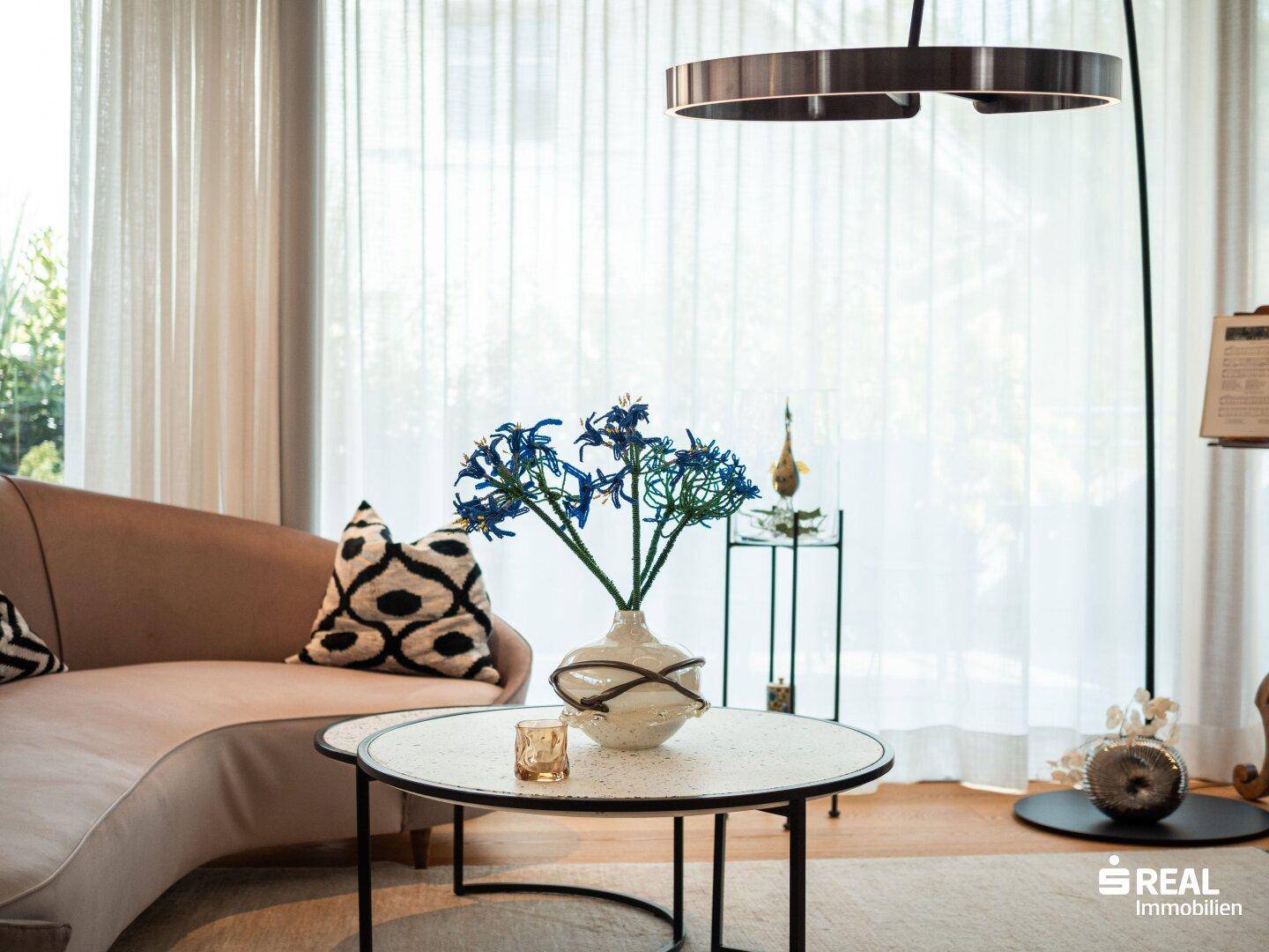 Elegantes Sofa mit Kissen und Couchtisch im hellen Wohnzimmer mit großen Fenstern.